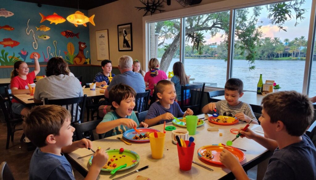 A lively dining scene at Aunt Catfish's on the River in Port Orange, Florida, showcasing a family enjoying a cheerful meal. In the foreground, a table filled with colorful, toy-themed plates and playful utensils, surrounded by children laughing and enjoying their food. In the middle ground, a cozy restaurant interior adorned with whimsical decor like fish-shaped lights and vibrant murals of aquatic life. In the background, large windows reveal a scenic river view with trees swaying gently in the breeze. The lighting is warm and inviting, creating a joyful, carefree atmosphere. The camera angle captures the action from a slightly elevated perspective, emphasizing the fun and excitement of dining out for kids.